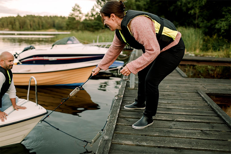 Woman standing on a pier helping man pull in a small boat